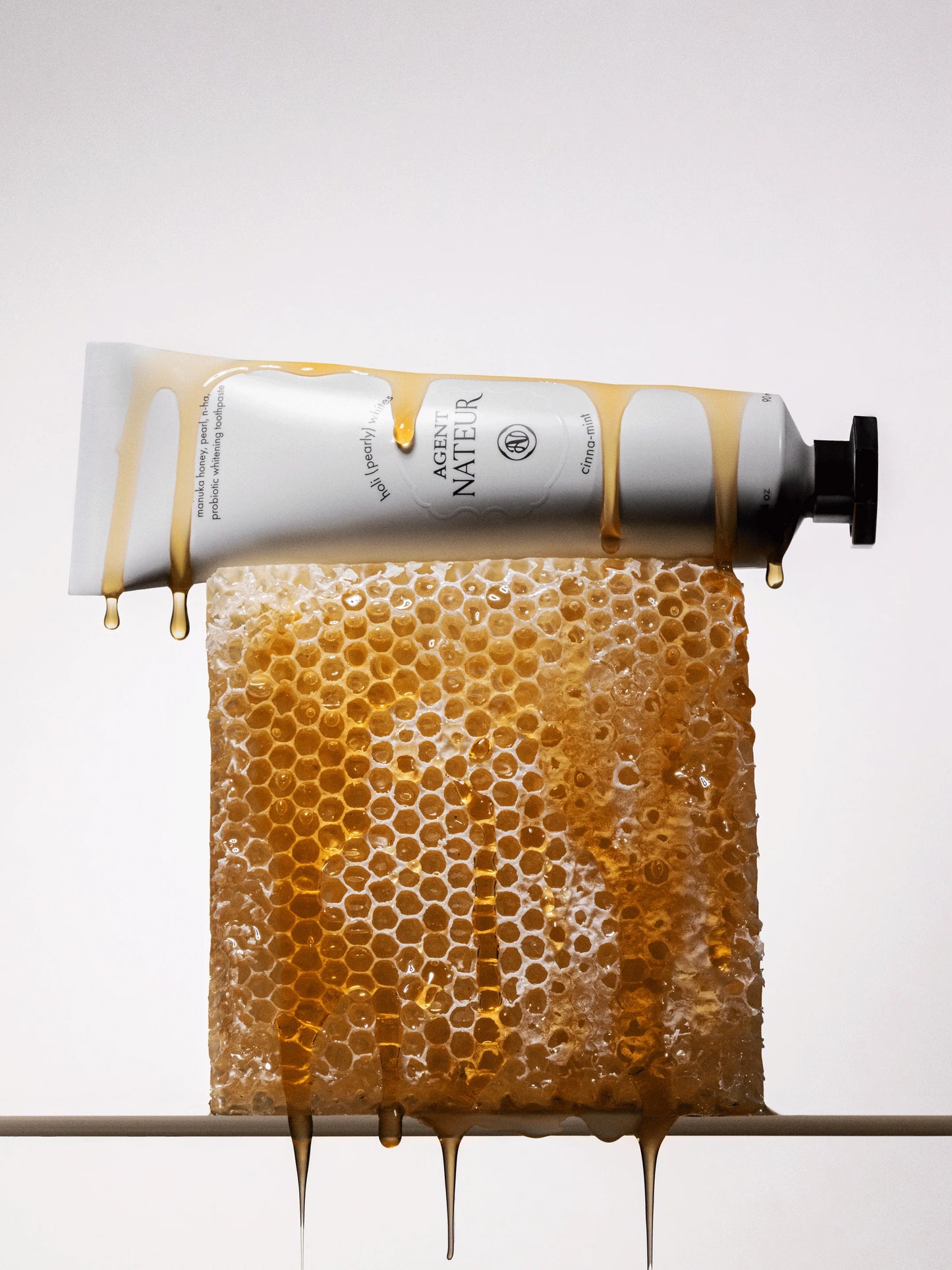Tube of honey with honeycomb and honey dripping on a white background