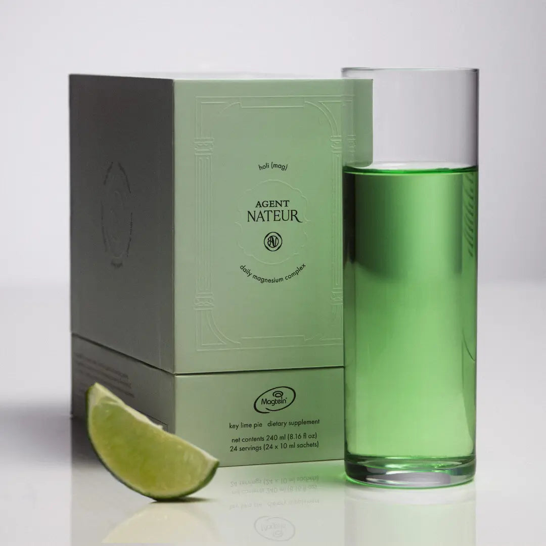 Green bottle of Agent Nateur supplement with packaging and lime wedge on a white background