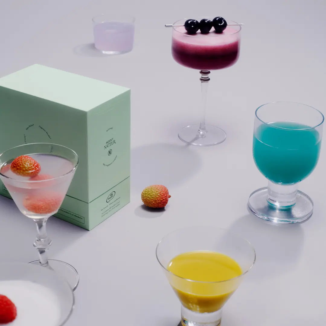 Assorted colorful cocktails in glassware on a light surface with a green box.