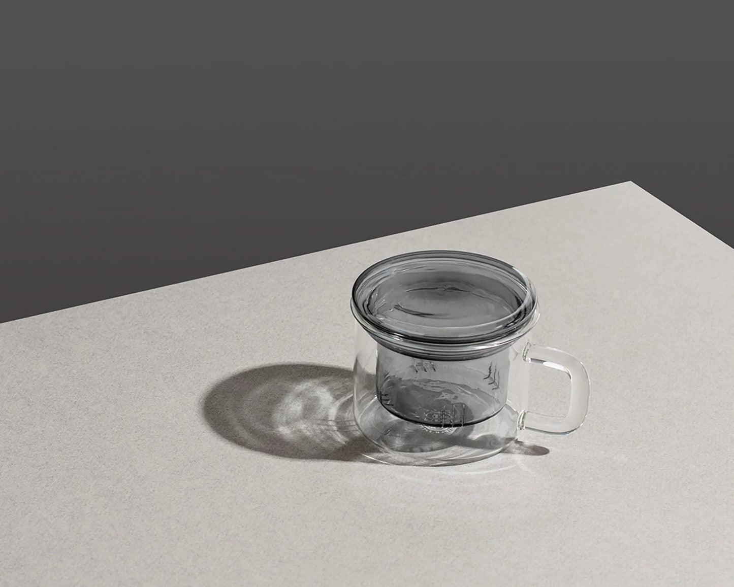Clear glass tea infuser on a light gray surface with a dark gray background