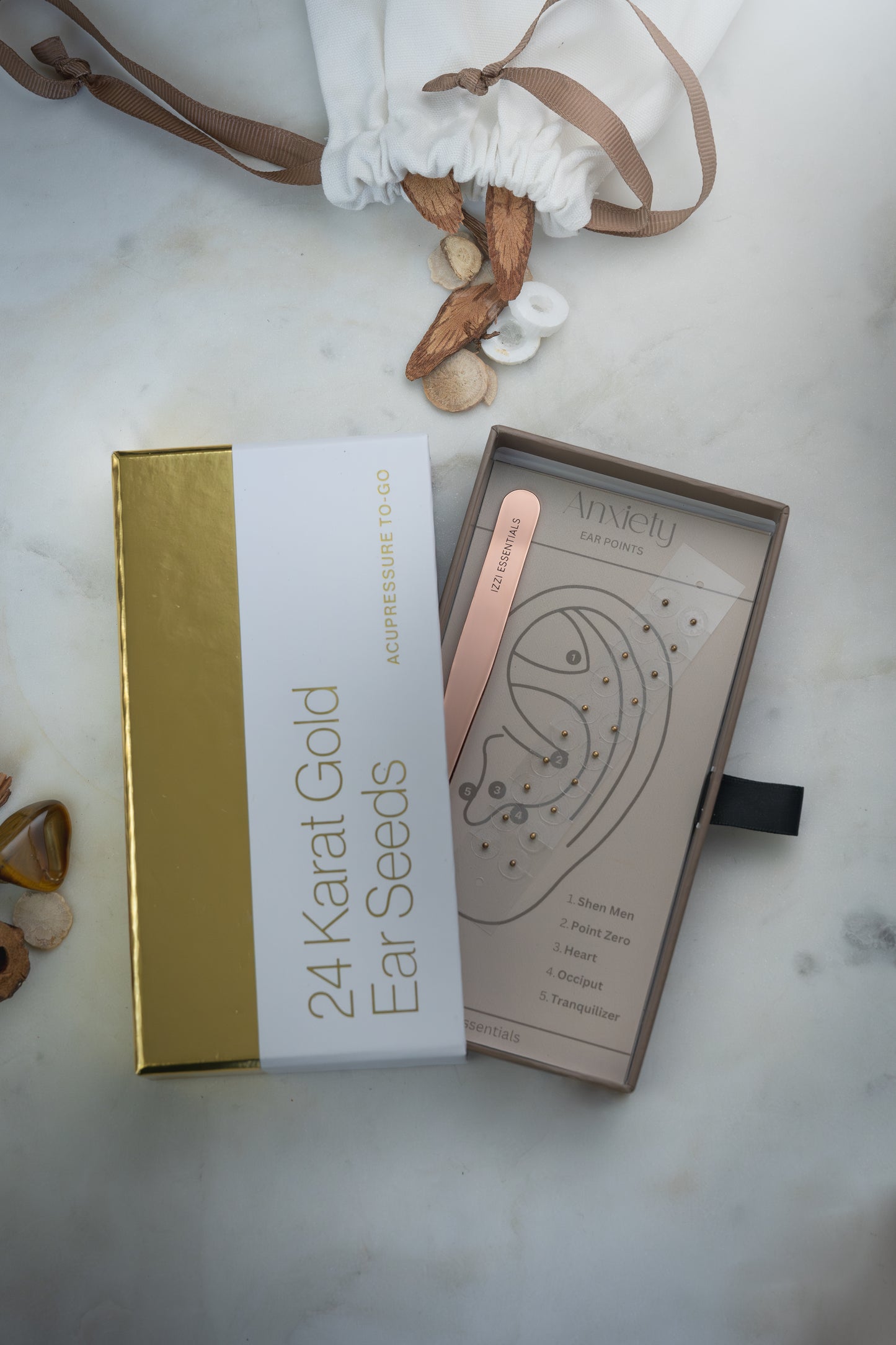 24 Karat Gold Ear Seeds packaging on a marble surface with decorative elements.