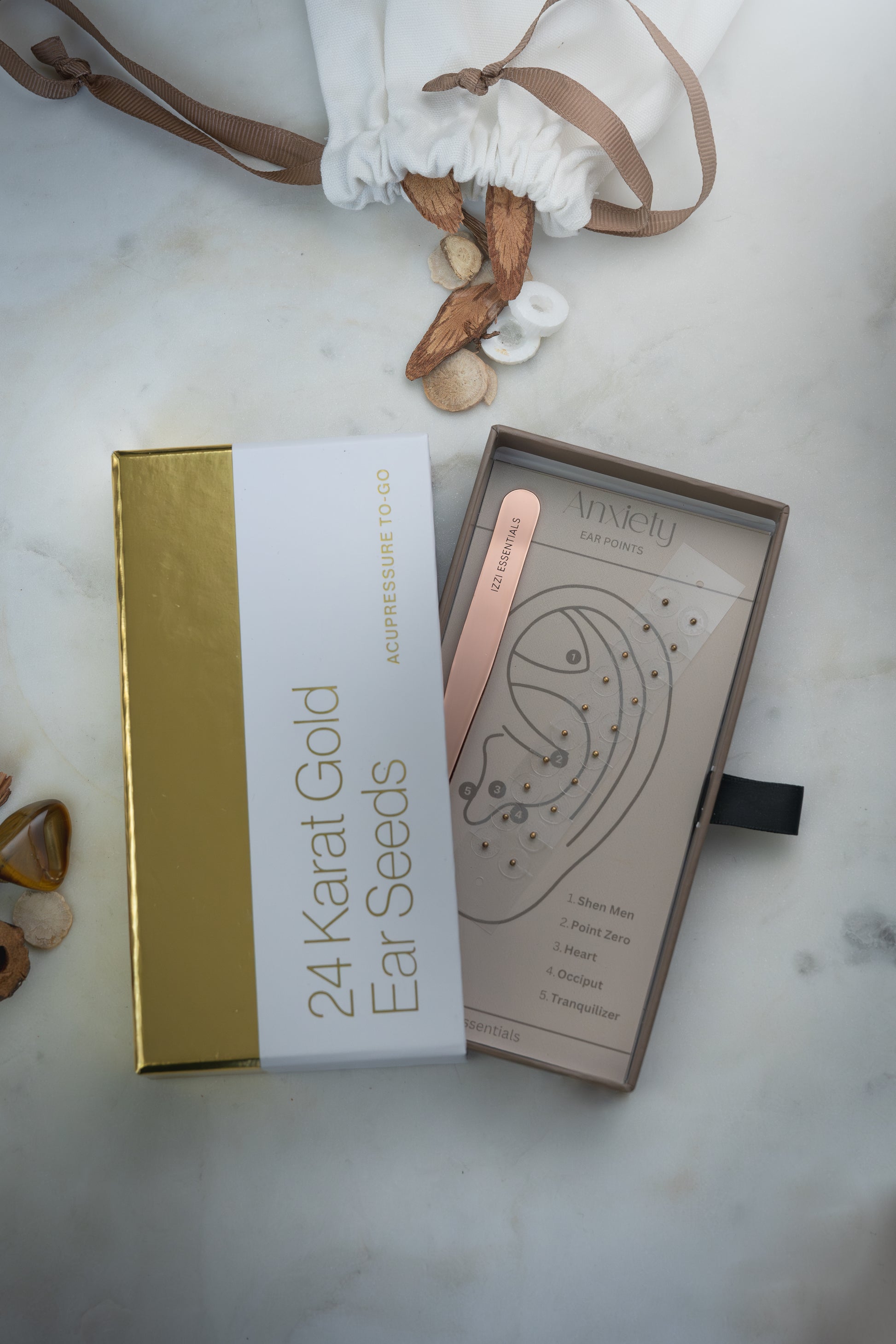 24 Karat Gold Ear Seeds packaging on a marble surface with decorative elements.