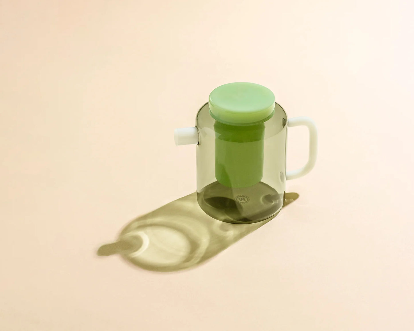Green glass container with a white handle on a beige background