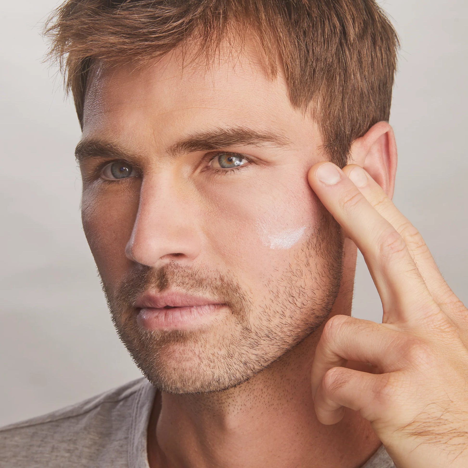 Man applying cream to his face with a neutral background