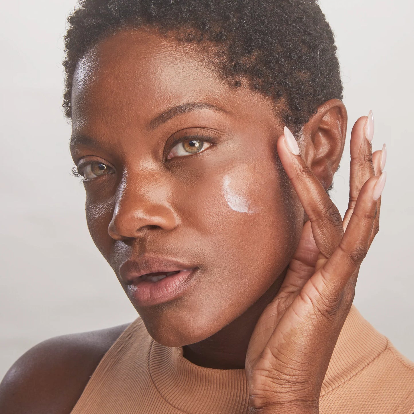 Woman applying cream to her face with a neutral background