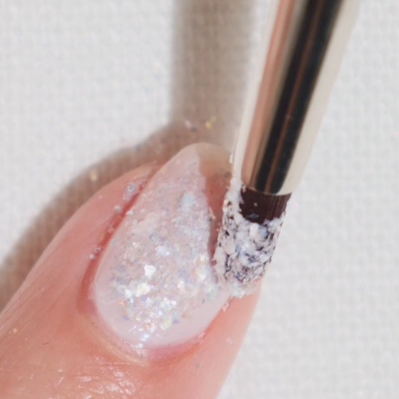 Close-up of a glittery nail polish being applied with a brush.