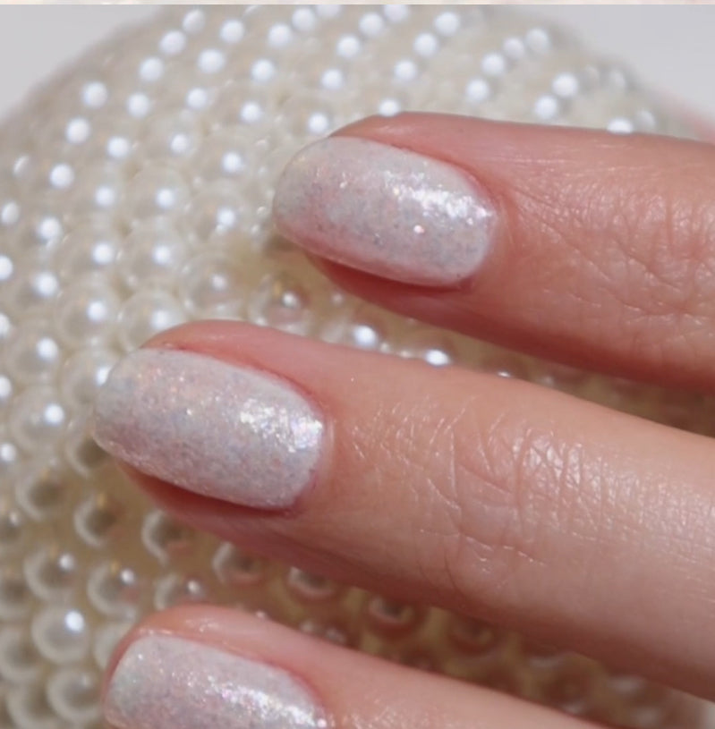 Close-up of a hand with glittery nail polish against a textured white background