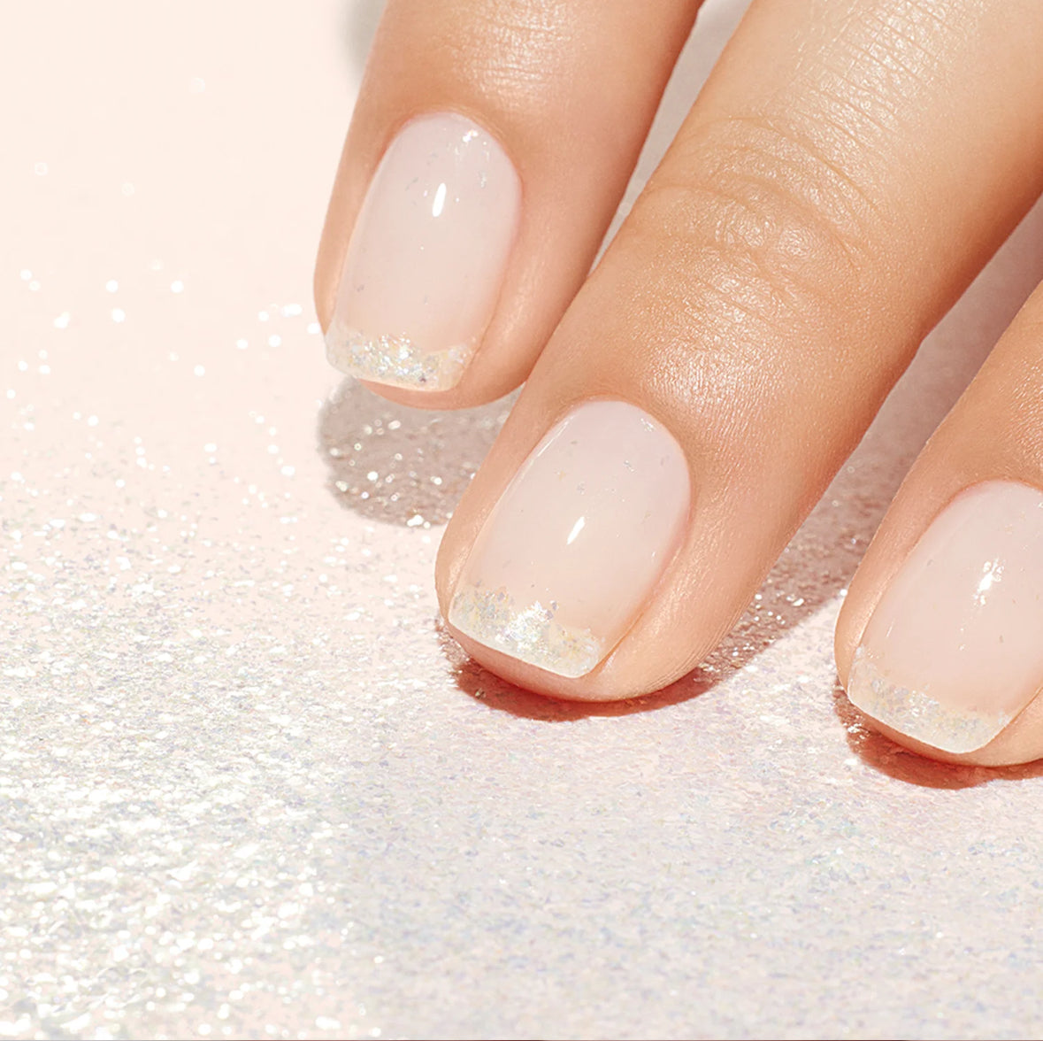 Close-up of a hand with light pink nail polish on a textured white background