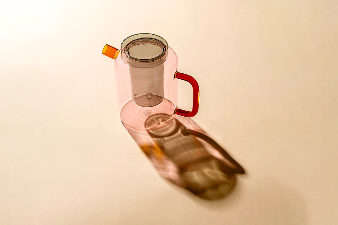 Pink glass carafe with a red handle on a beige background