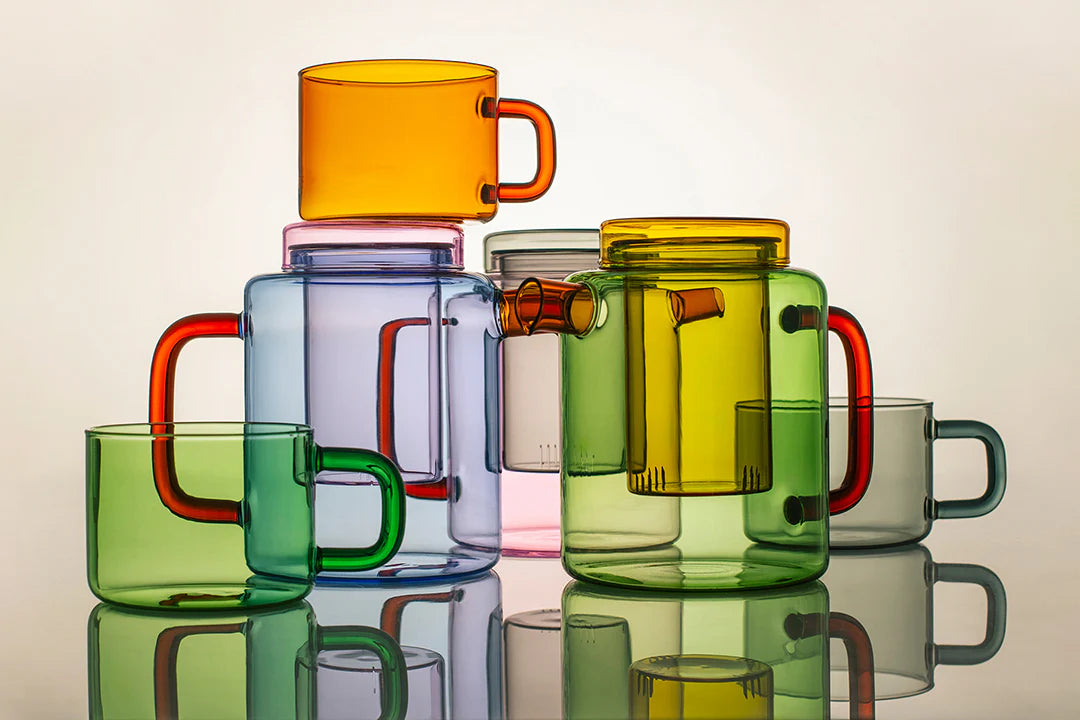 Colorful glass mugs stacked on a reflective surface with a neutral background