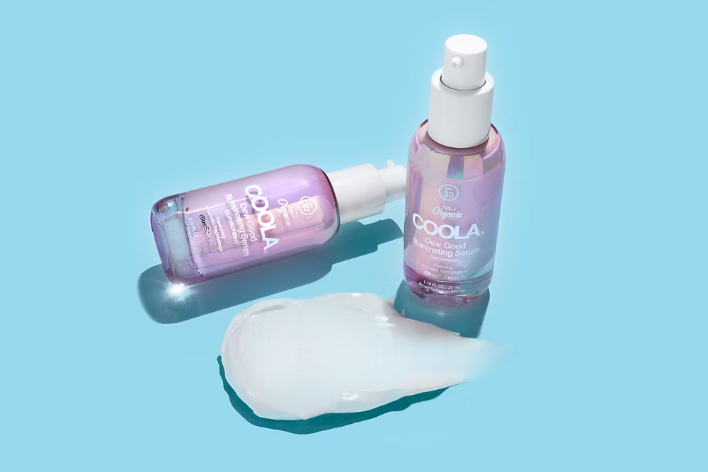 Two bottles of Coola sunscreen lotion on a blue background